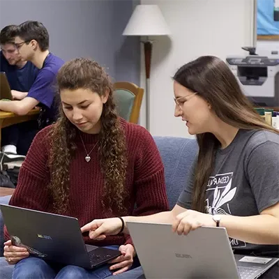 Writing Center tutor helping a student with laptops open.